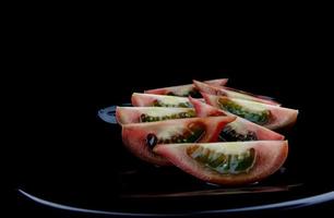 Ripe cumato tomatoes cut with slices on a black plate. photo