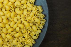 Macaroni raw in white bowl on black plate. photo