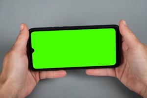 hands holding the phone horizontally, green chroma key mockup on smartphone photo