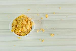 imagen cierre el desayuno de cereales con copos de maíz en un tazón blanco sobre una mesa de madera. foto