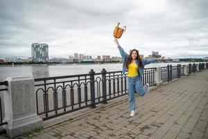 chica feliz con ropa de mezclilla saltando con mochila en la mano foto