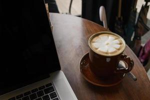 taza de café y computadora portátil en la mesa de madera en la cafetería. concepto de negocio foto
