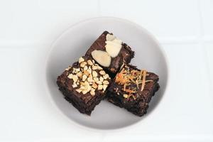 Homemade chocolate fudge brownie with mix topping, close up, served on plate, isolated on white background. Selective focus image. photo