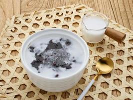 Bubur Ketan Hitam, Indonesian dessert. Black glutinous rice porridge with coconut milk, sugar and pandan leaf. Served in a white bowl on a wooden table. photo