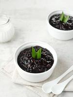 Bubur Ketan Hitam, Indonesian dessert. Black glutinous rice porridge with coconut milk, sugar and pandan leaf. Served in a white bowl on a wooden table. photo