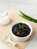 Bubur Ketan Hitam, Indonesian dessert. Black glutinous rice porridge with coconut milk, sugar and pandan leaf. Served in a white bowl on a wooden table. photo