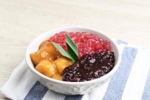 Bubur Madura, Indonesian traditional dessert. Black glutinous rice with Candil and Sagu Mutiara porridge and pandan leaf. Served in white bowl on wooden table. Selective focus. photo