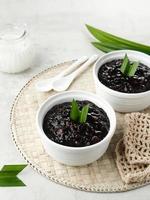 Bubur Ketan Hitam, Indonesian dessert. Black glutinous rice porridge with coconut milk, sugar and pandan leaf. Served in a white bowl on a wooden table. photo