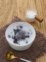 Bubur Ketan Hitam, Indonesian dessert. Black glutinous rice porridge with coconut milk, sugar and pandan leaf. Served in a white bowl on a wooden table. photo