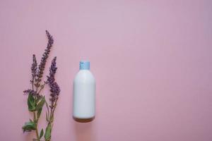 White plastic bottle with lavender flowers on a violet background. Copy space. Top view photo