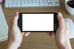 manos de mujer sosteniendo la pantalla vacía del teléfono inteligente en el trabajo de escritorio de madera foto