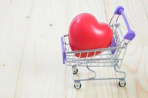 Shopping cart and heart on wood table background photo