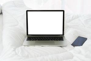 computadora portátil con pantalla en blanco y teléfono inteligente en la cama, concepto de vacaciones foto