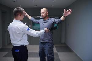 Security guard with a metal detector making body searching procedure on man photo