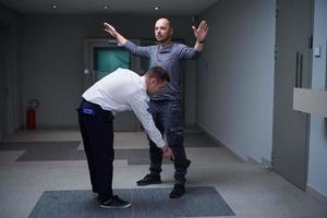 Security guard with a metal detector making body searching procedure on man photo