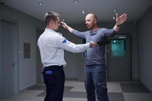 Security guard with a metal detector making body searching procedure on man photo