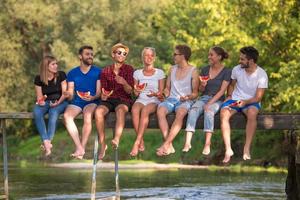 friends enjoying watermelon while sitting on the wooden bridge photo