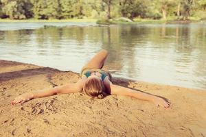 chica en bikini verde relajándose en la orilla del río foto