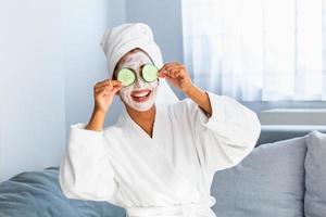 Woman with facial mask and cucumber slices in her hands. Beautiful young woman with facial mask on her face holding slices of fresh cucumber. Young woman with clay facial mask holding cucumber slices photo