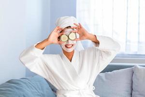 Woman with facial mask and cucumber slices in her hands. Beautiful young woman with facial mask on her face holding slices of fresh cucumber. Young woman with clay facial mask holding cucumber slices