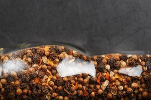 A mixture of peppercorns seasoning and salt in a transparent mill close-up photo