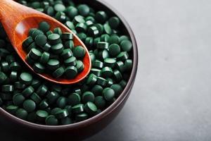 Vitamins from spirulina in a wooden cup with a wooden spoon on a dark background photo