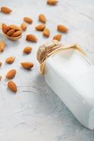 Almond milk in a glass bottle on a light background with a scattering of seed kernels and a wooden spoon. photo