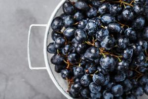 uvas negras dulces en un recipiente de metal sobre un fondo de textura oscura. foto