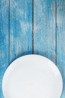un plato blanco redondo vacío sobre una mesa de madera azul. foto
