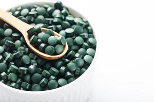 Organic spirulina tablets in a white cup with a wooden spoon photo