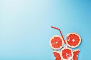 Grapefruit slices and ice cubes with a straw on a blue background in the shape of a cocktail. photo