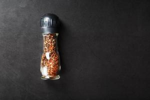 A mixture of seasonings, spices and herbs in a glass mill on a black background.
