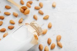 Milk from organic almonds in a transparent bottle with a scattering of seeds and a wooden spoon on a light background photo