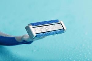 Shaving machine with three blades on a blue background with water drops in close-up photo