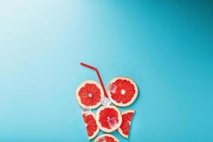 Grapefruit slices and ice cubes with a straw on a blue background in the shape of a cocktail. photo