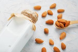 Almond milk in a glass bottle on a light background with a scattering of seed kernels and a wooden spoon. photo