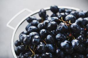 uvas negras dulces en un recipiente de metal sobre un fondo de textura oscura. foto