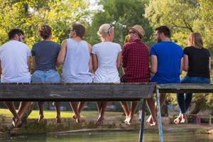 rear view of friends enjoying watermelon while sitting on the wooden bridge photo