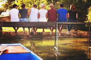 vista trasera de amigos disfrutando de sandía mientras están sentados en el puente de madera foto