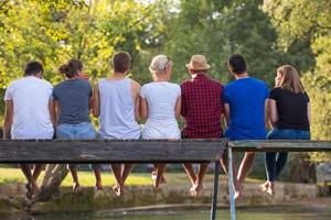 vista trasera de amigos disfrutando de sandía mientras están sentados en el puente de madera foto