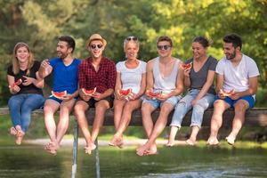 friends enjoying watermelon while sitting on the wooden bridge photo