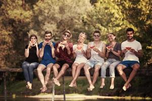 friends enjoying watermelon while sitting on the wooden bridge photo