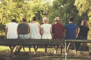 rear view of friends enjoying watermelon while sitting on the wooden bridge photo