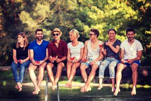 amigos disfrutando de la sandía mientras están sentados en el puente de madera foto