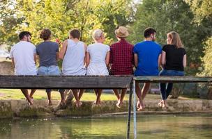 rear view of friends enjoying watermelon while sitting on the wooden bridge photo