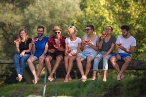 friends enjoying watermelon while sitting on the wooden bridge photo