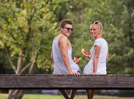 couple enjoying watermelon while sitting on the wooden bridge photo