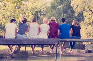 rear view of friends enjoying watermelon while sitting on the wooden bridge photo