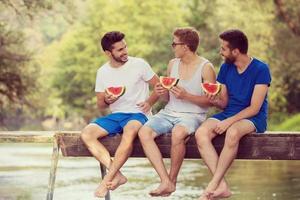 hombres disfrutando de la sandía mientras se sientan en el puente de madera foto