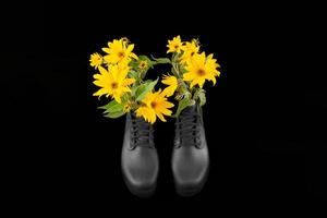 botas de plataforma de mujer negra con ramo de flores amarillas de alcachofa de Jerusalén, fondo negro foto